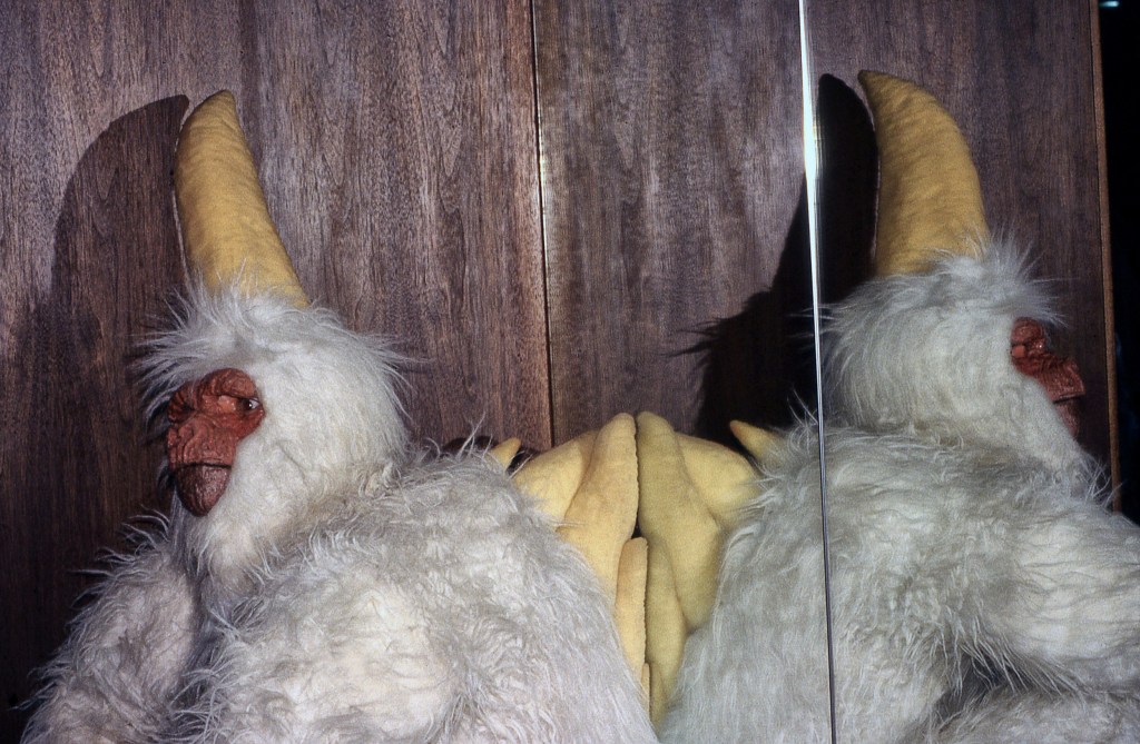 A convention attendee dressed as a Mugato and reflected in a mirrored door.