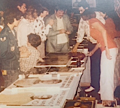 A dealers' room at Miamicon in 1975, with a long table of merchandise and fans gathered around James Doohan.